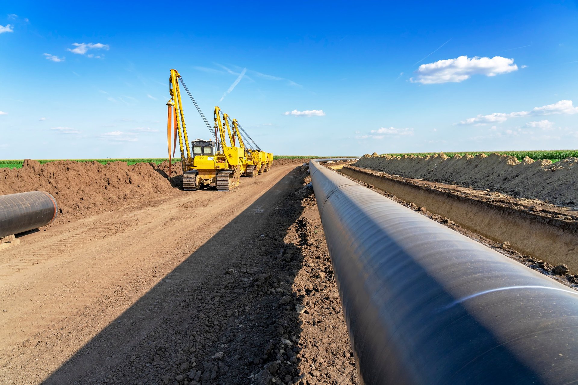 Steel line pipe laid beside an excavated trench at a pipeline construction site, ready for welding