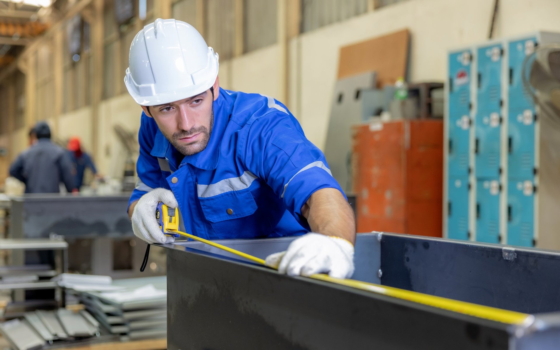 Workers checking the size of steel stock before it goes to a cutting machine in a factory