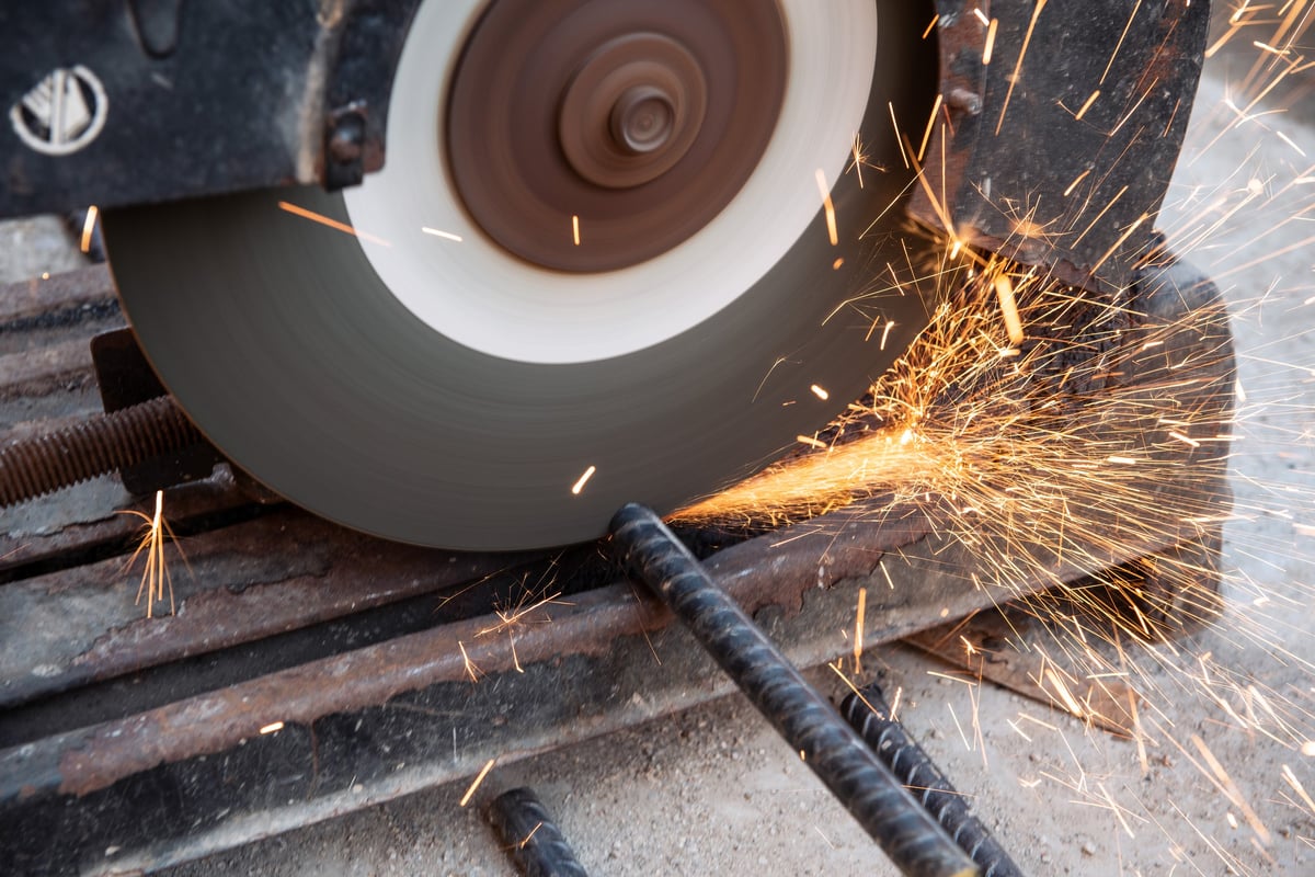 Cutting equipment working a reinforcing bar in a fabrication yard, illustrating the fabrication step where minimum bend and cut provisions must be checked against the grade.