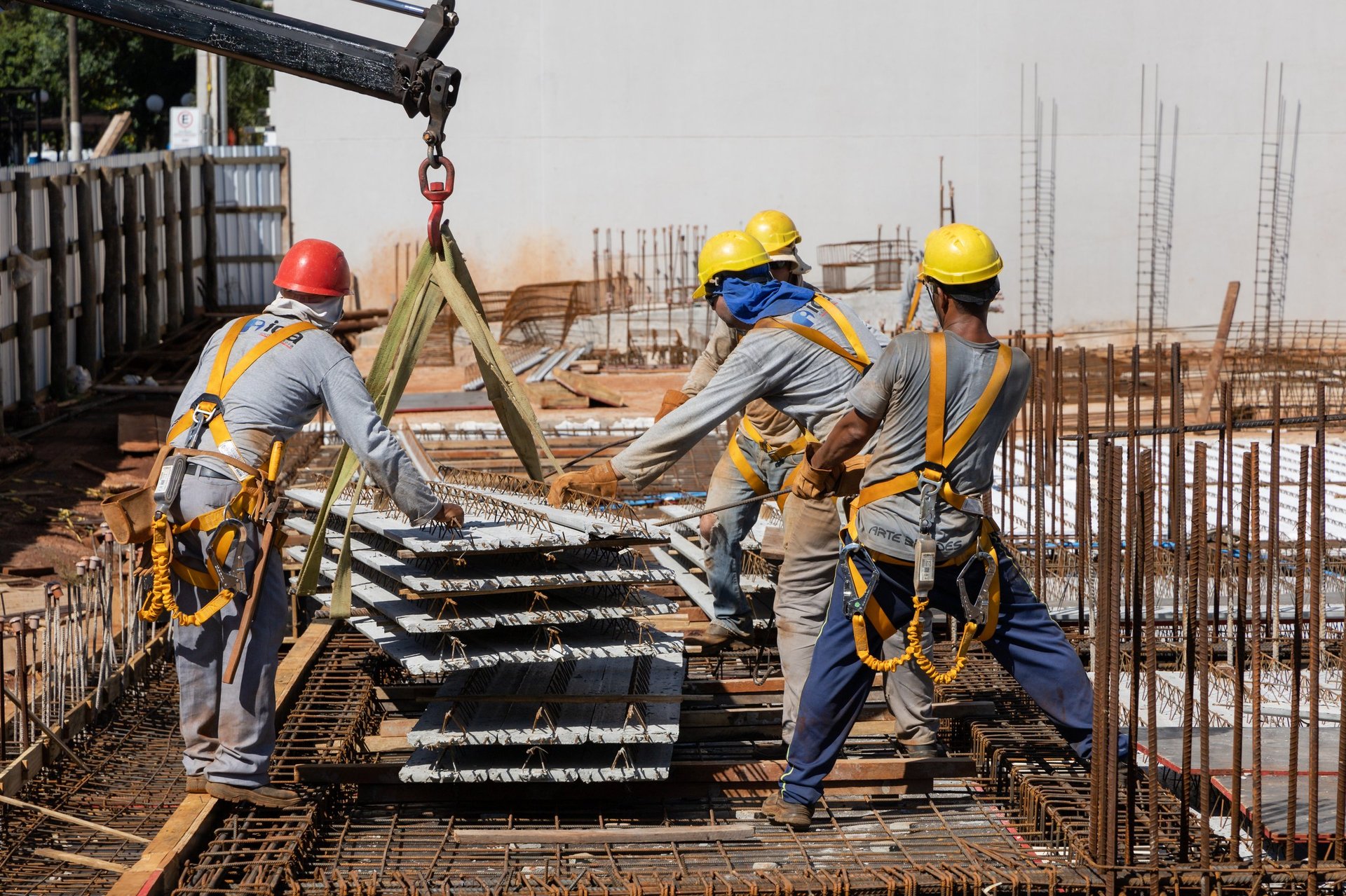 Construction workers placing steel and concrete slab sections on a building under construction, illustrating heavy main reinforcement being installed at the work face.
