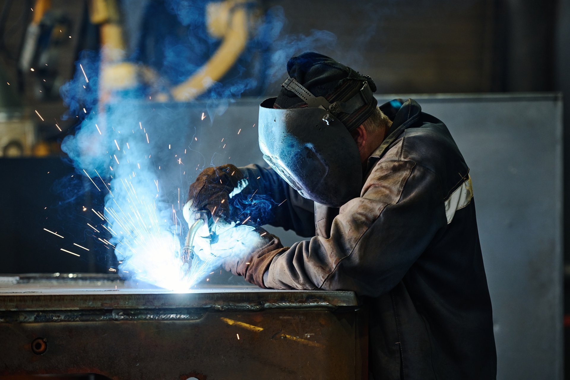 Fabricator welding a steel component in a workshop, with sparks from the welding arc
