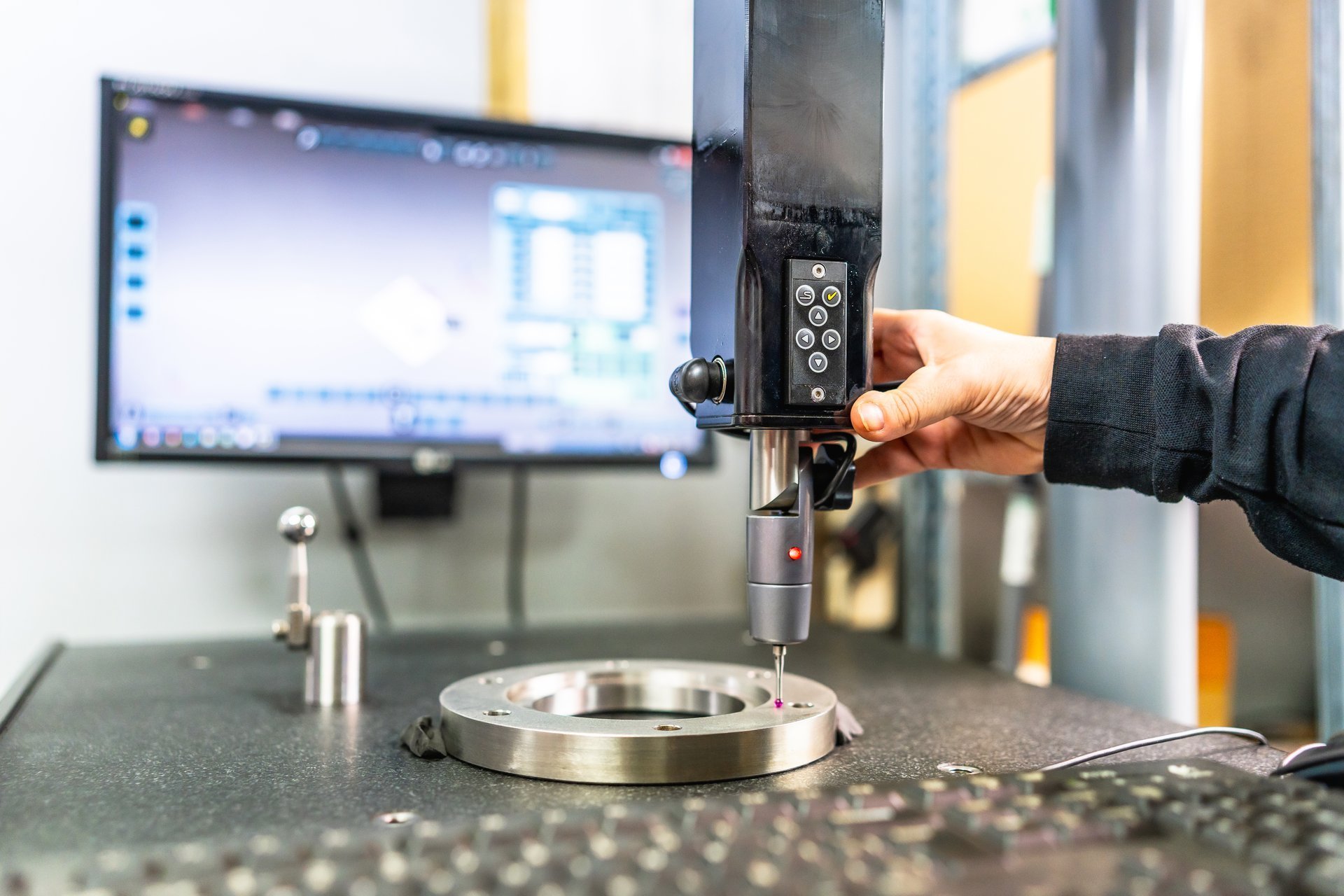 Technician operating a dimensional measuring and verification machine beside coated metal components in a workshop