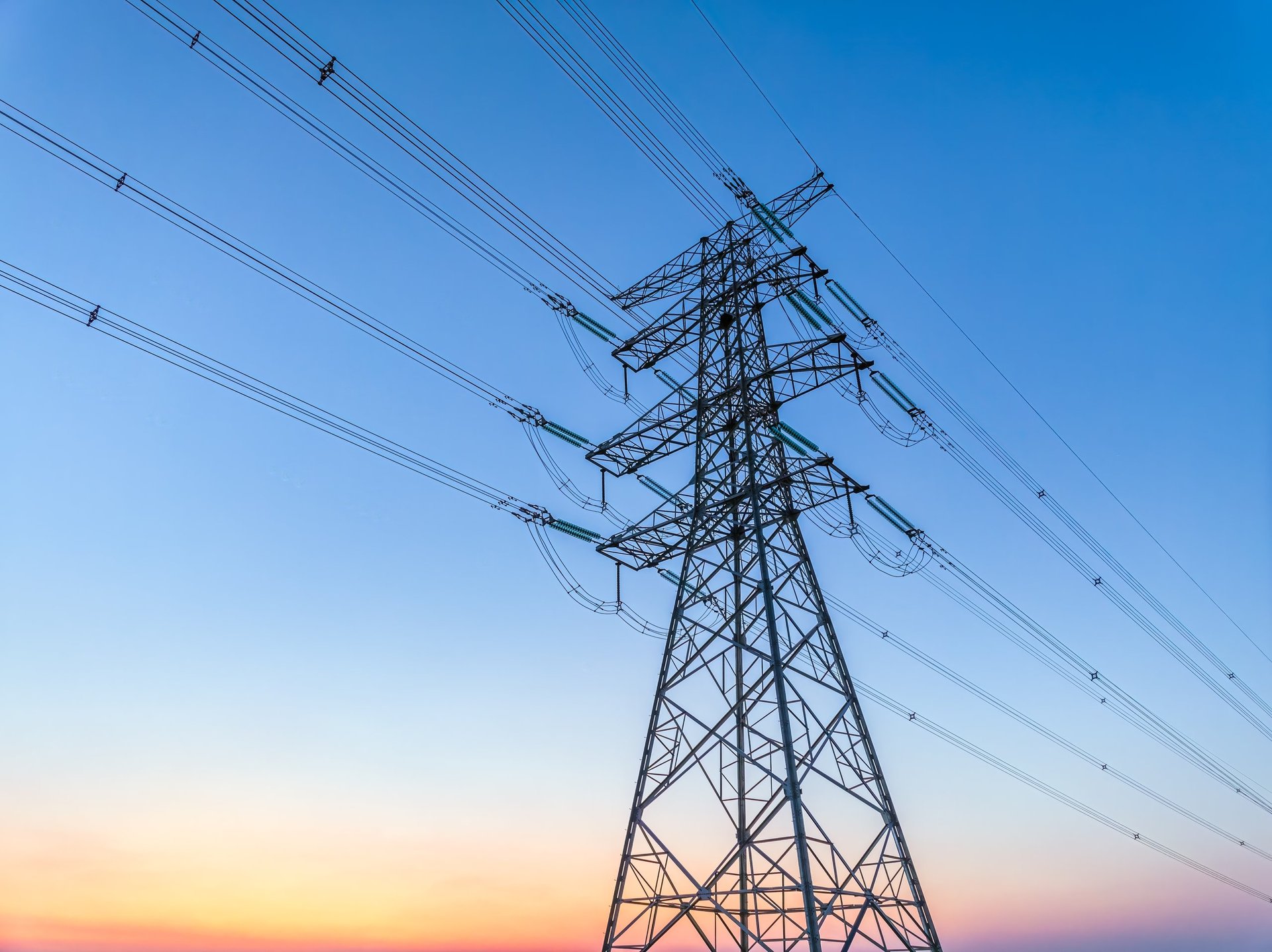 High-voltage transmission tower standing in open landscape at sunset