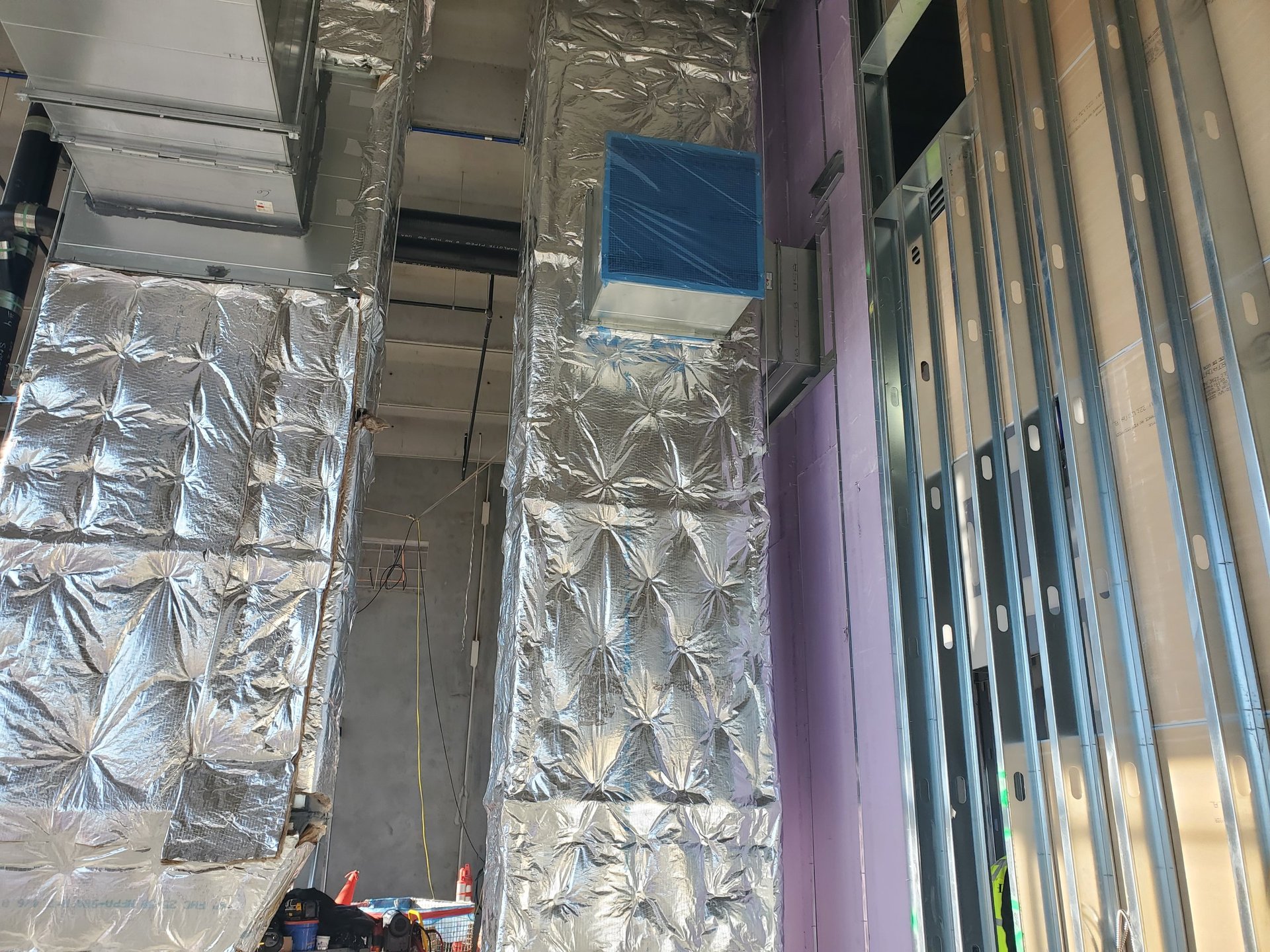 Galvanized ductwork runs installed across an exposed ceiling on a construction site