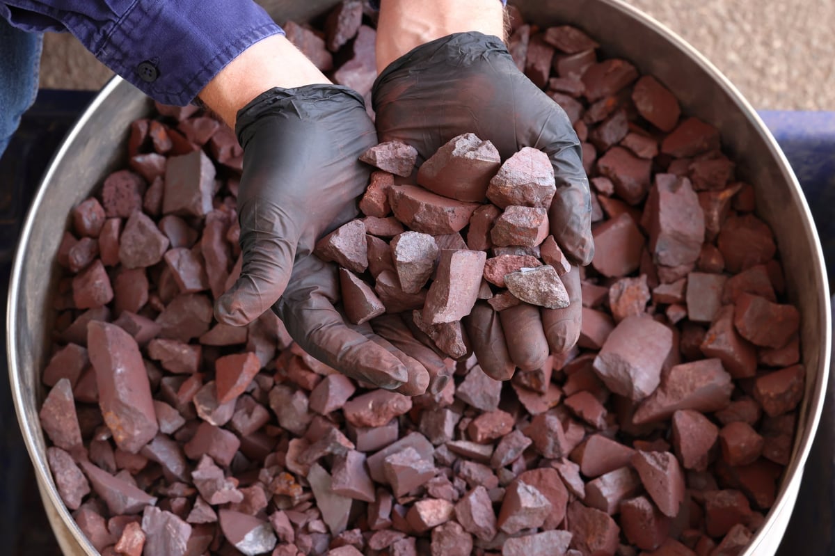 Hand holding a sample of high-grade hematite iron ore, shown for the appearance of the feed material.