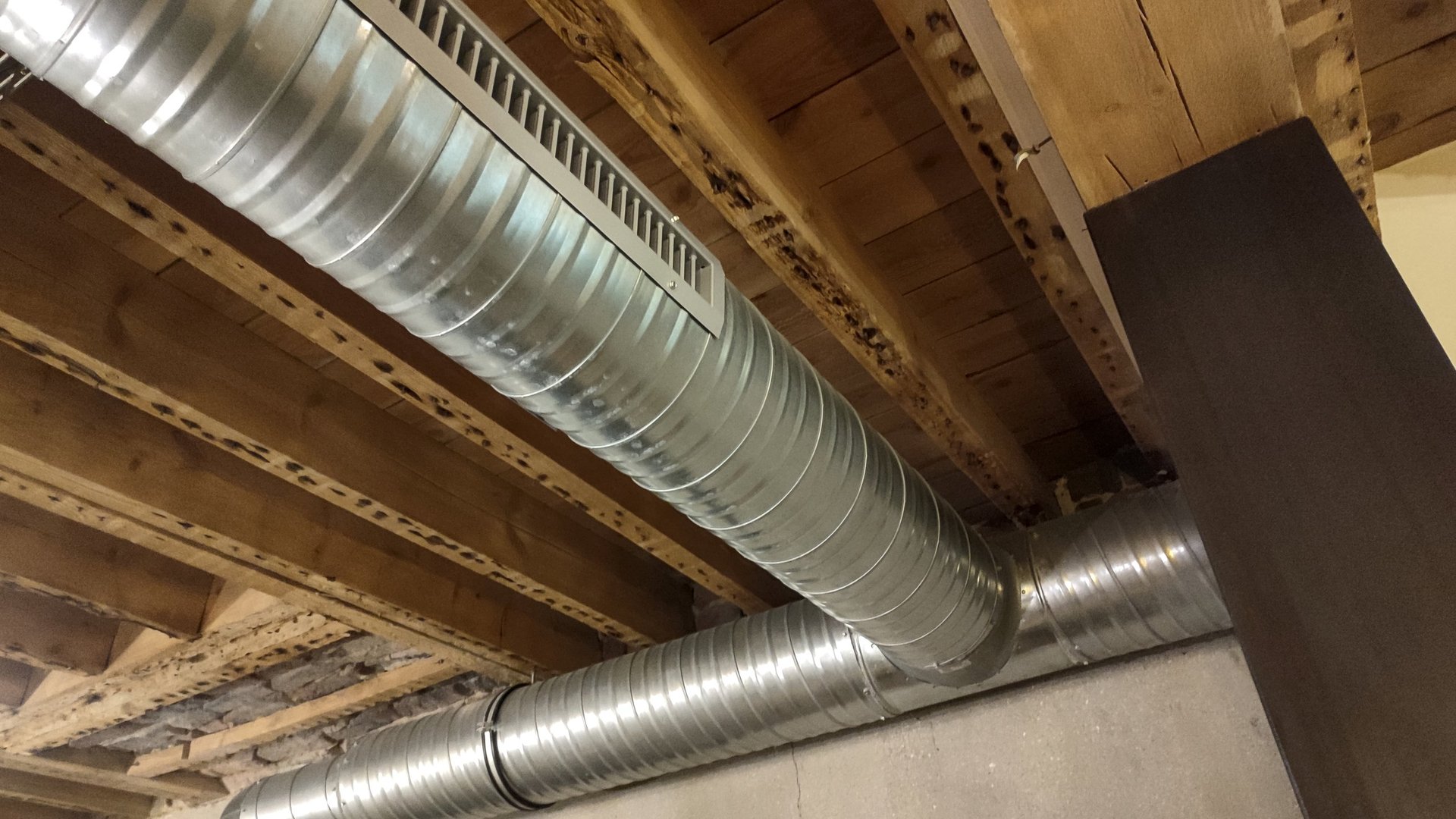 Exposed galvanized metal duct run fixed below a ceiling, showing formed sections and joints