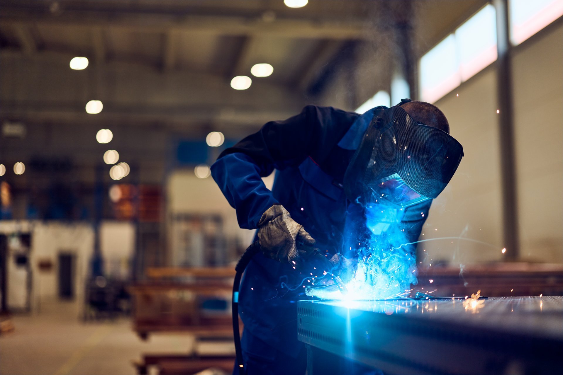 Welder in protective gear joining a steel component with sparks in a fabrication workshop