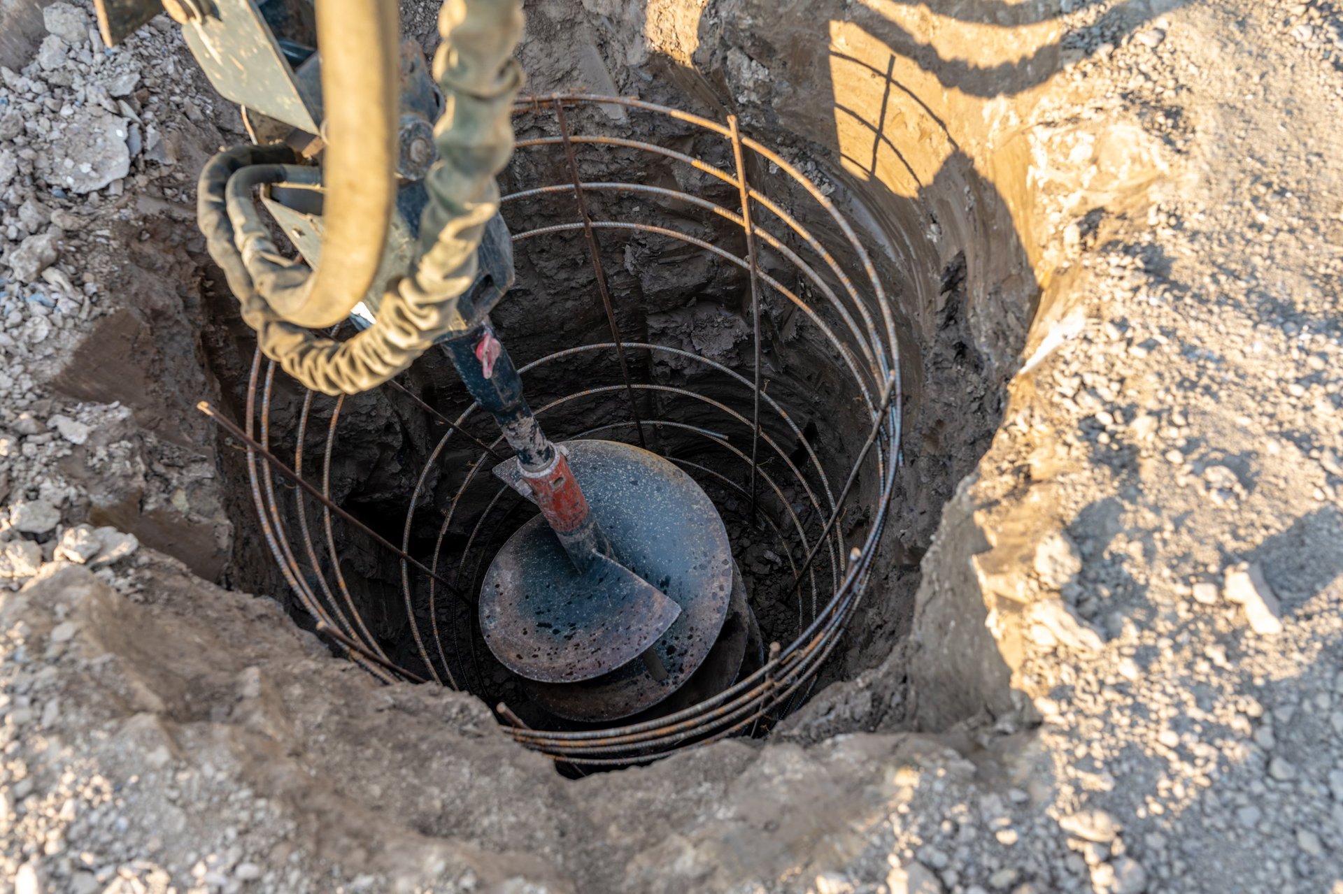 Construction equipment drilling a vertical hole for a cast-in-place reinforced concrete pile foundation, illustrating the deep foundation work where the heaviest main bars are placed.