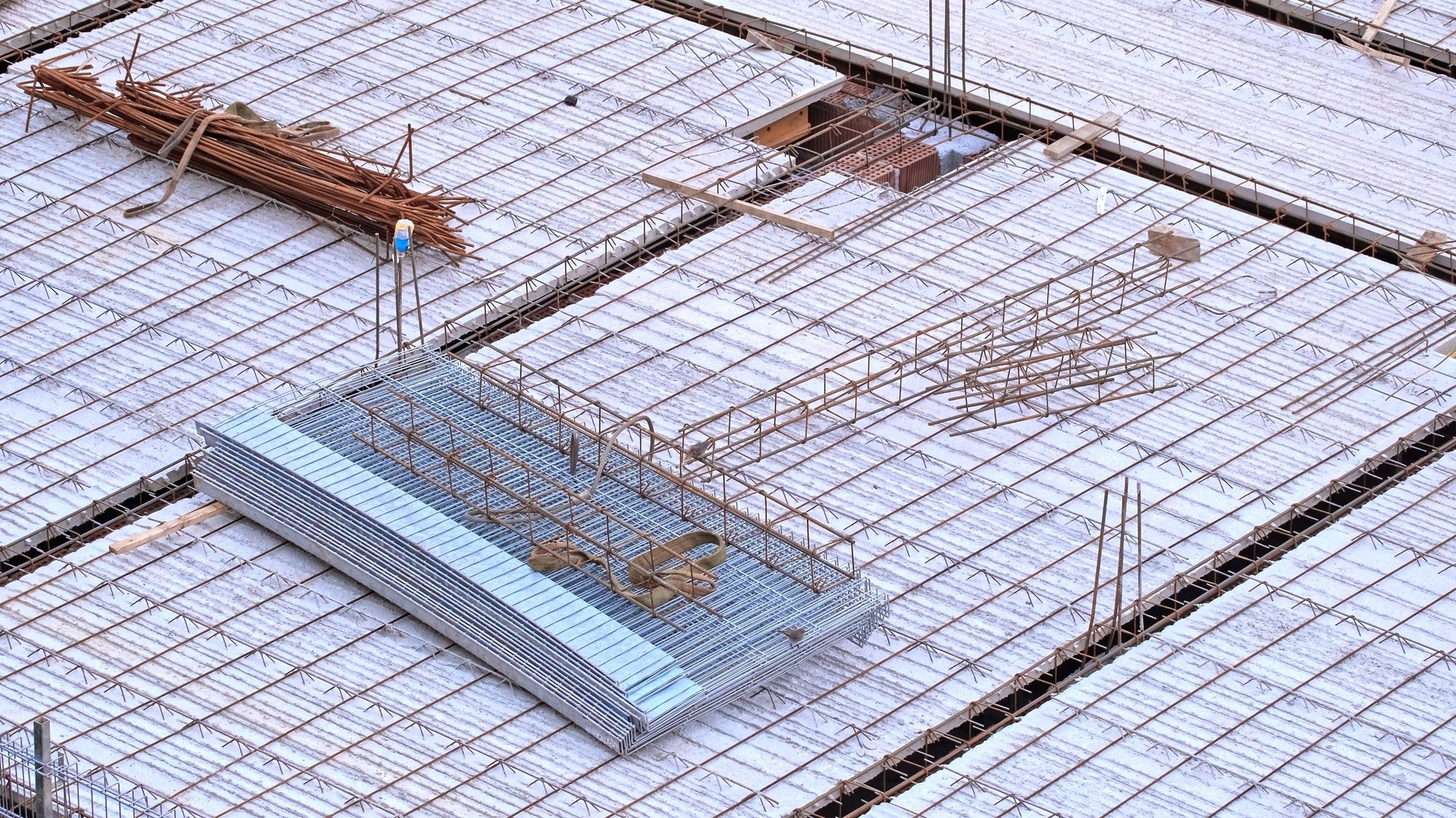 Rusty stirrup rebar reinforcement rods and precast concrete slab blocks on a building construction site, illustrating the repetitive bent small-diameter pieces an 8 mm order consists of.