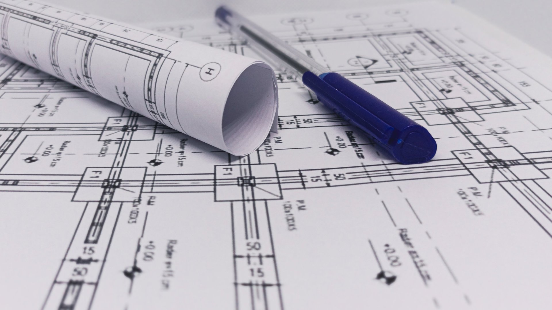 Rolled blueprint and pen on construction plans, the annotation and cross-reference motif behind Noor Deira Steel's steel comparison