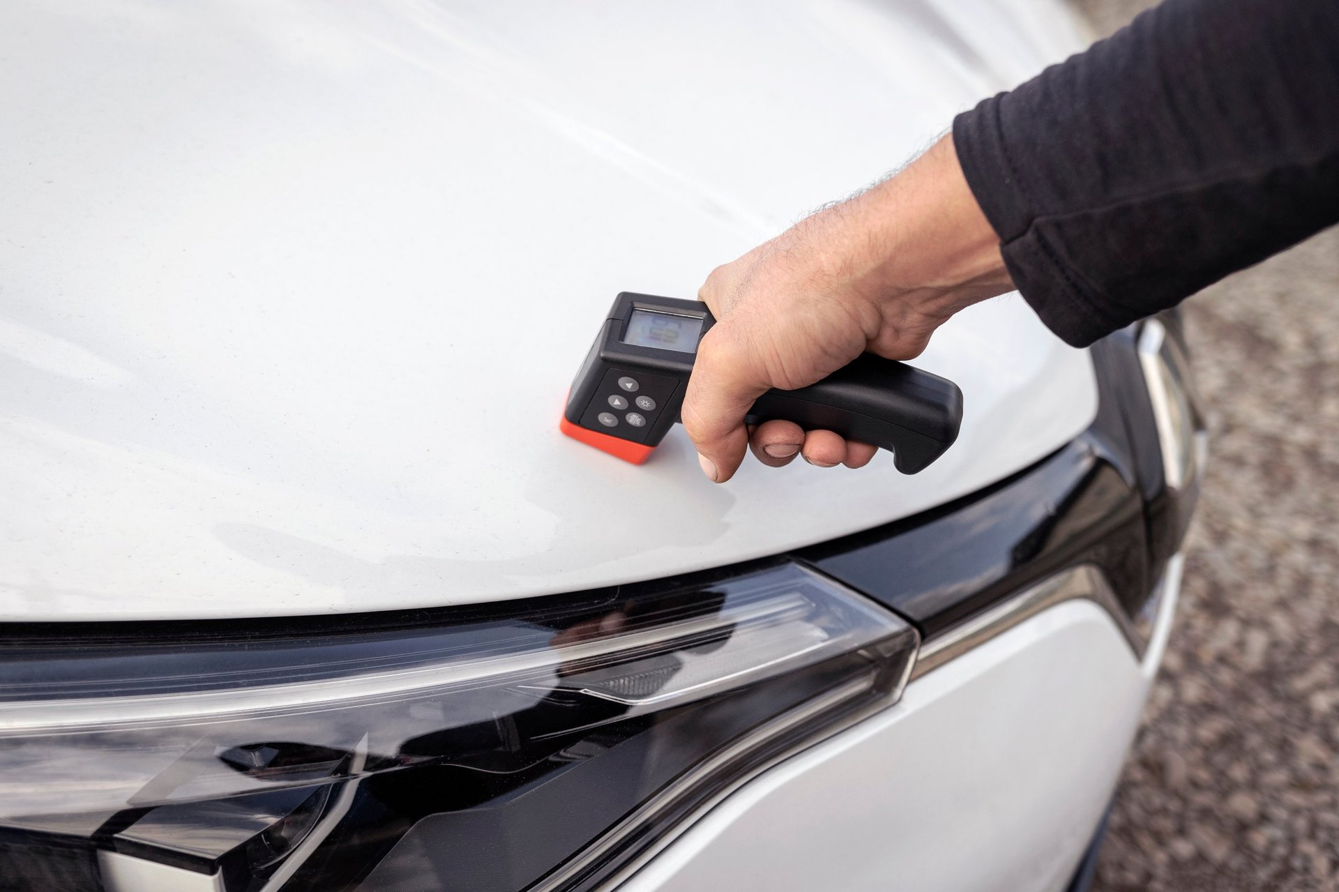 Handheld gauge measuring coating thickness on a painted metal surface