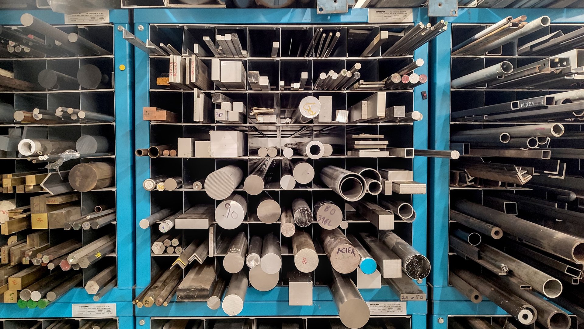 Steel bars of different profiles stored together in a workshop rack, showing plain and ribbed forms