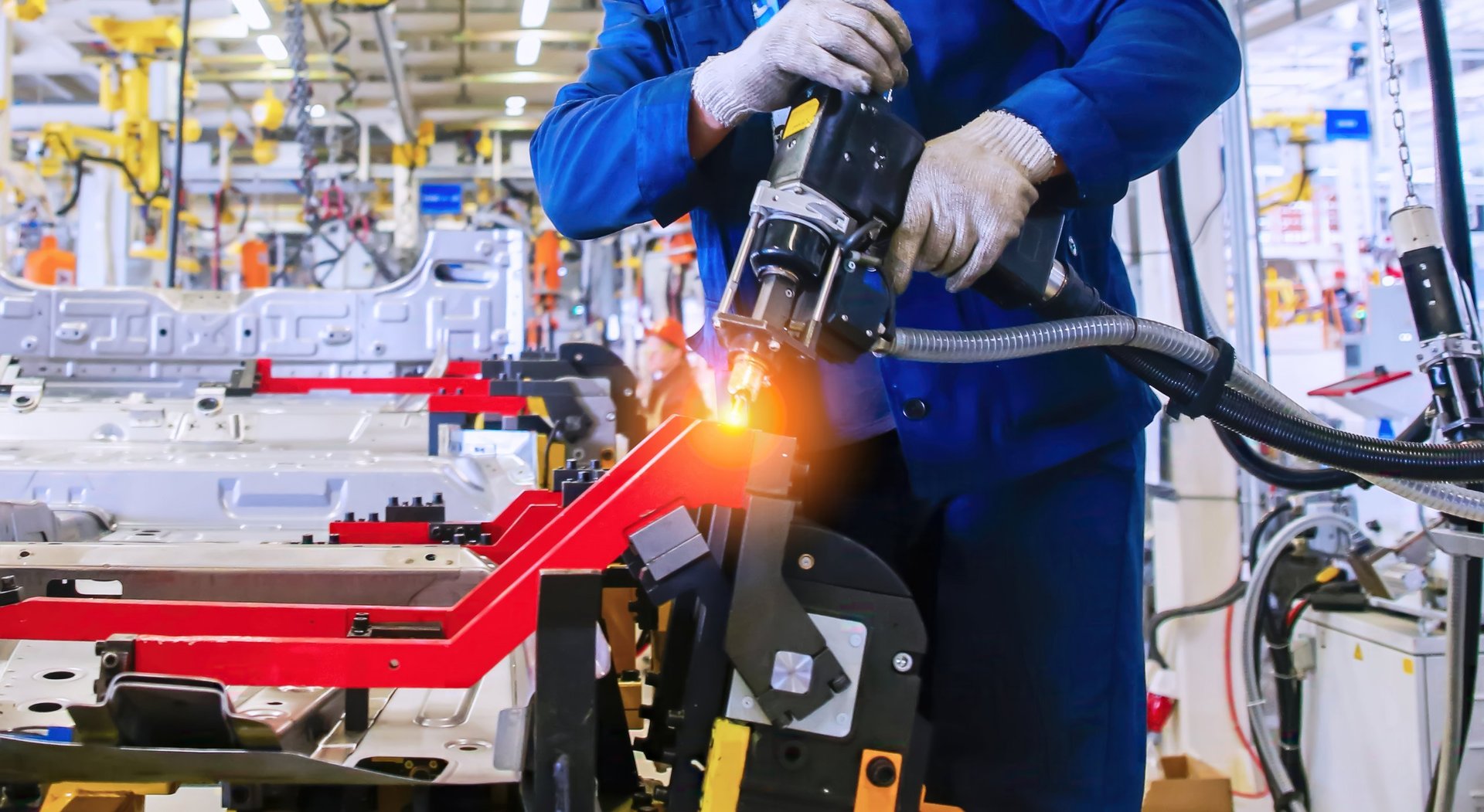 Workers assembling sheet metal vehicle components in a large manufacturing plant