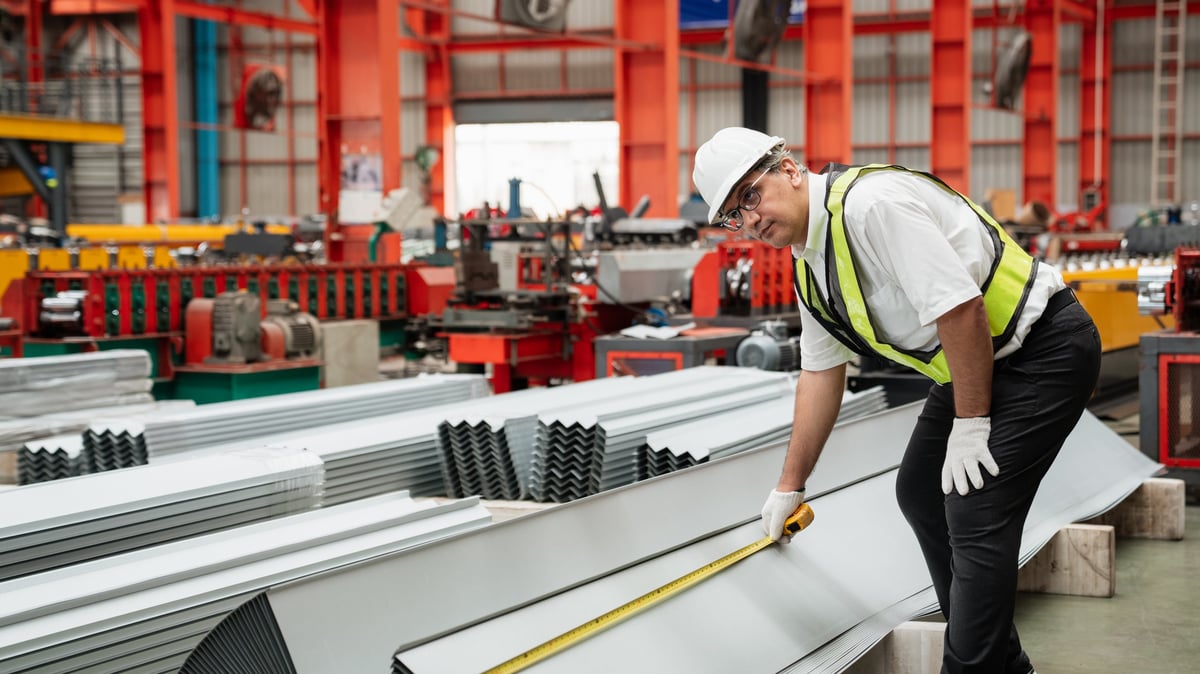 Workers checking steel sections against a specification on an inspection line