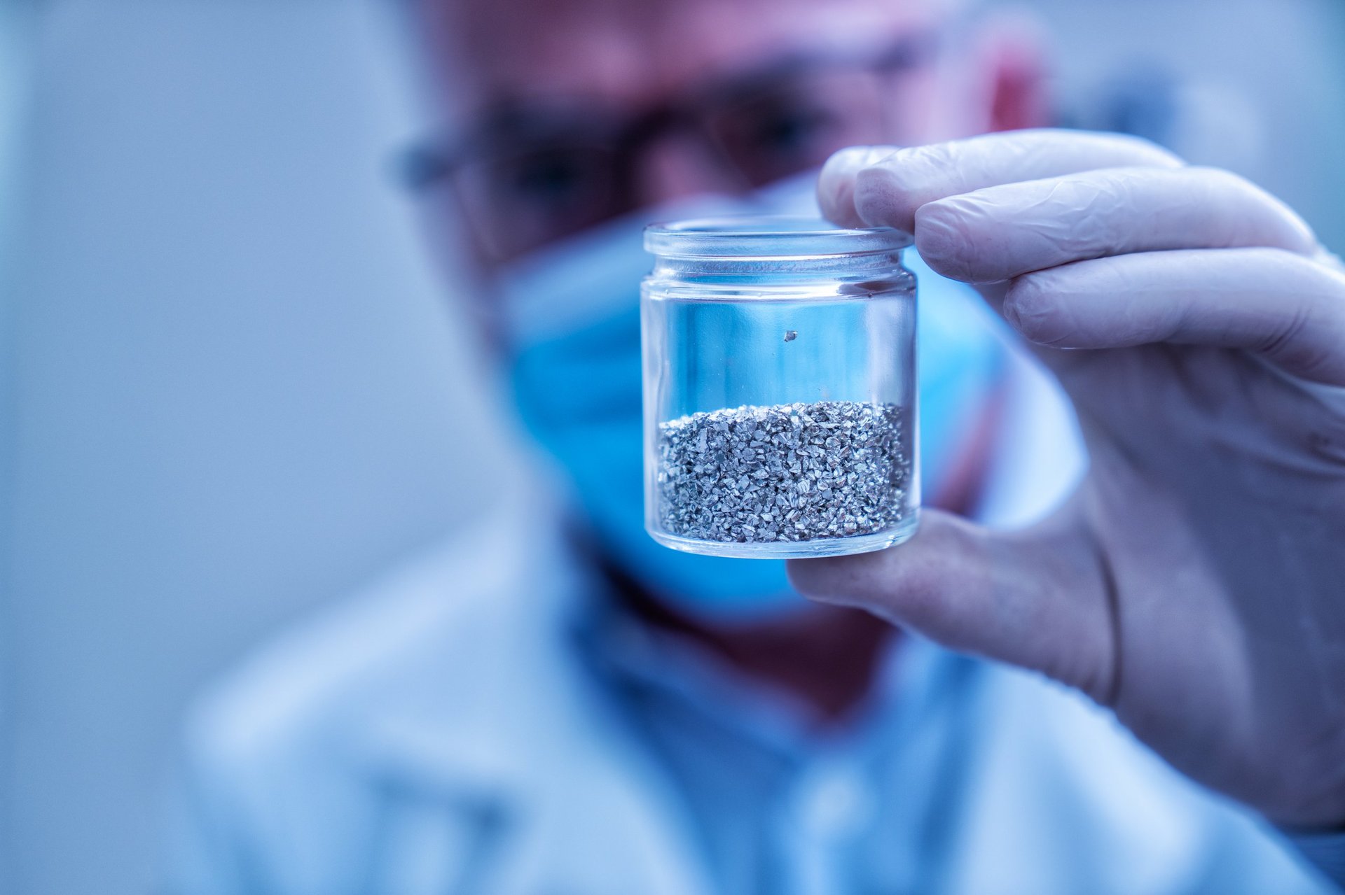 A laboratory technician examining a prepared mineral sample in a small container.