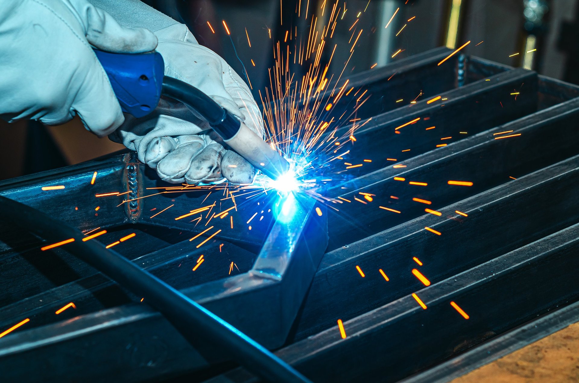 Fabricator welding a steel component with sparks in a workshop
