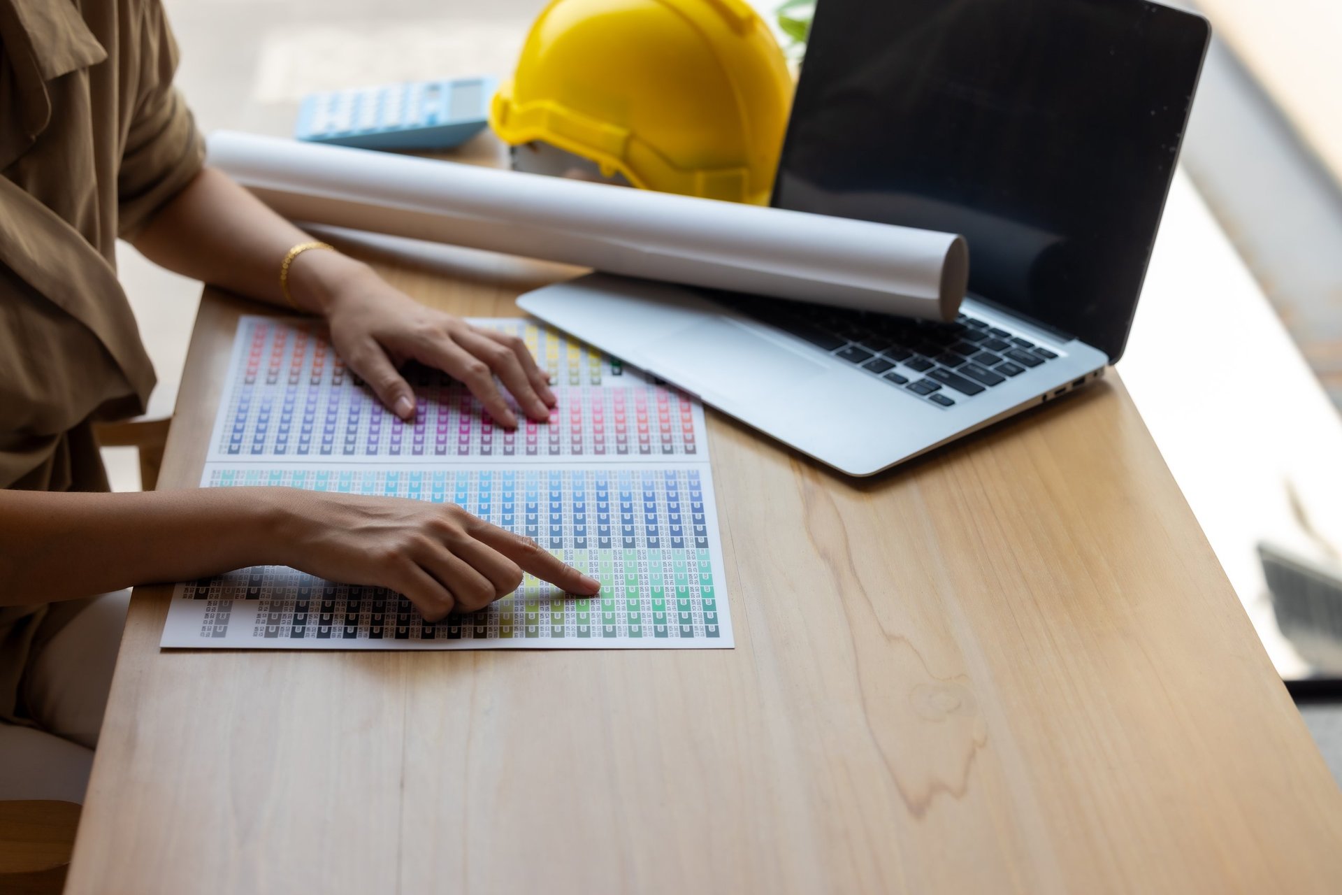 Quantity surveyor working at a desk with construction blueprints and a hard hat, measuring quantities against drawings before issuing an enquiry.