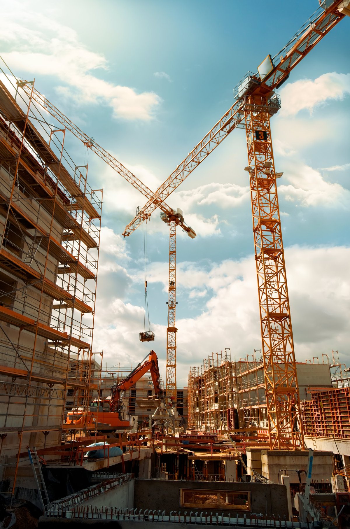 High-rise construction with tower cranes against the sky, illustrating the congested frames where code restrictions on high-strength reinforcement and splice rules matter most.