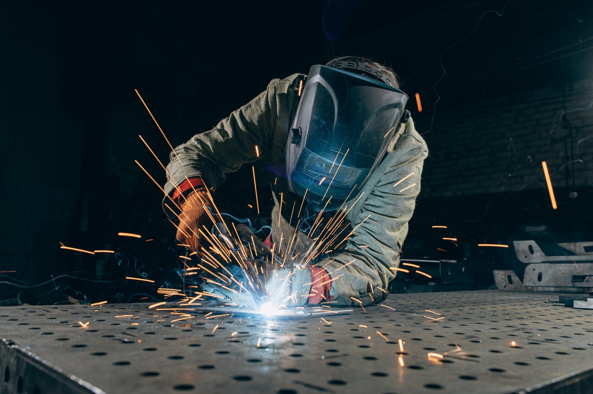 Welder joining steel with a torch, sparks visible, wearing protective gear in a workshop