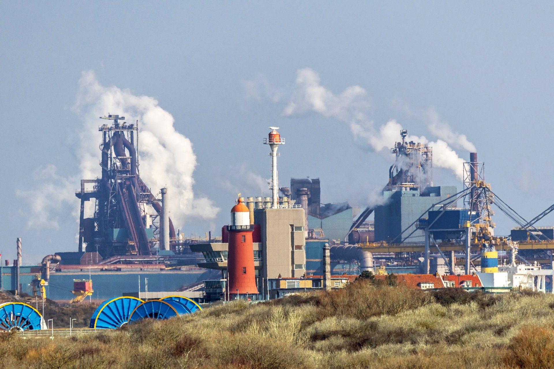 Steel plant releasing steam, representing the hot-rolling origin of the material