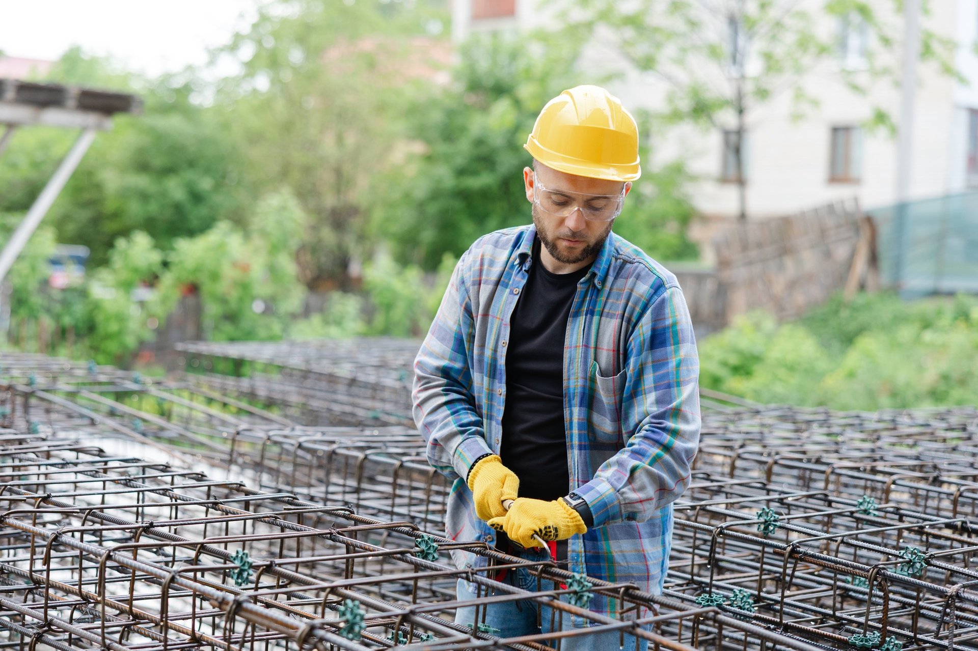 Builder inspecting a steel reinforcement cage on a foundation, checking that bars and links are arranged as the detailing drawings require.