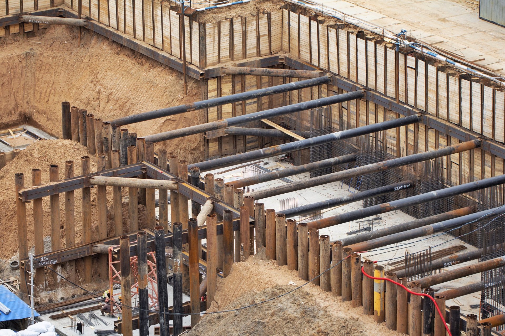 High-angle view of a deep construction pit reinforced with heavy steel struts and retaining walls, illustrating a heavy load path where large-diameter reinforcement is placed.