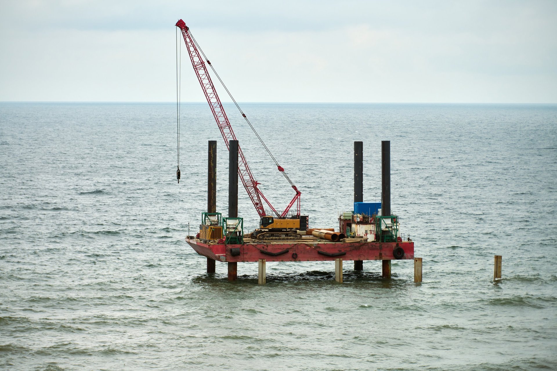 Heavy crane on a floating platform installing steel pilings in shallow water