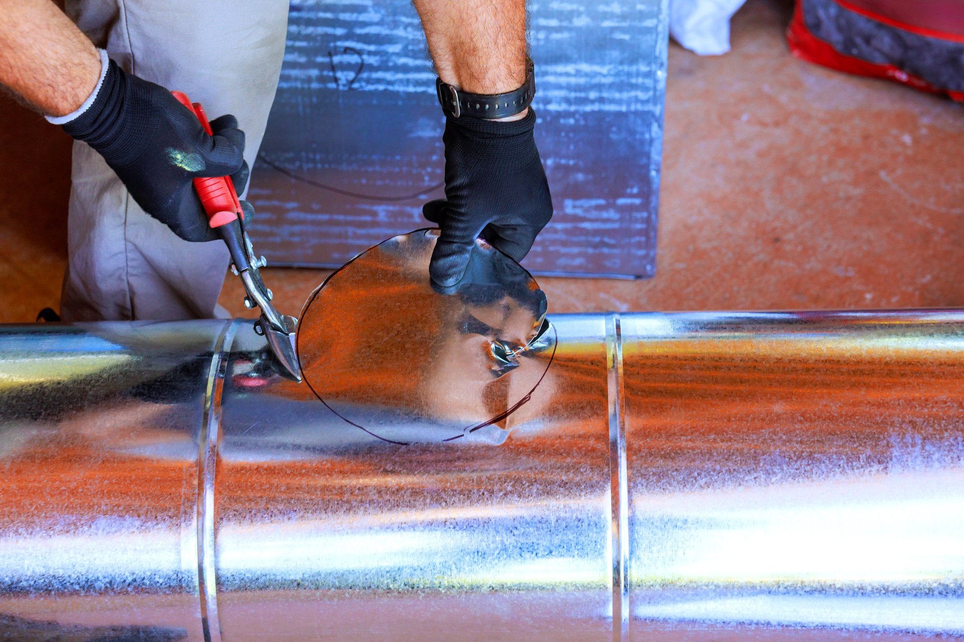Worker cutting a galvanized steel duct component with snips in a fabrication workshop