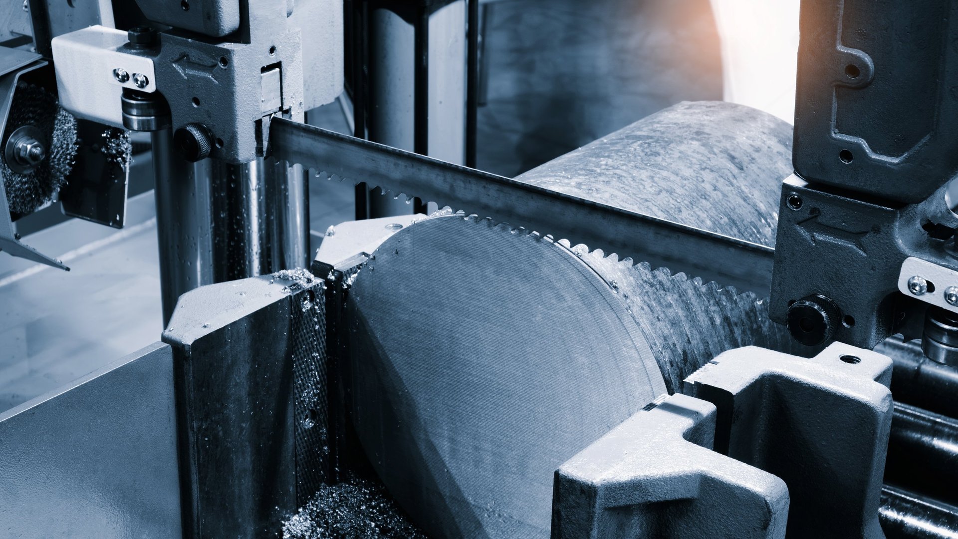 Automatic band saw cutting a metal section to length with coolant