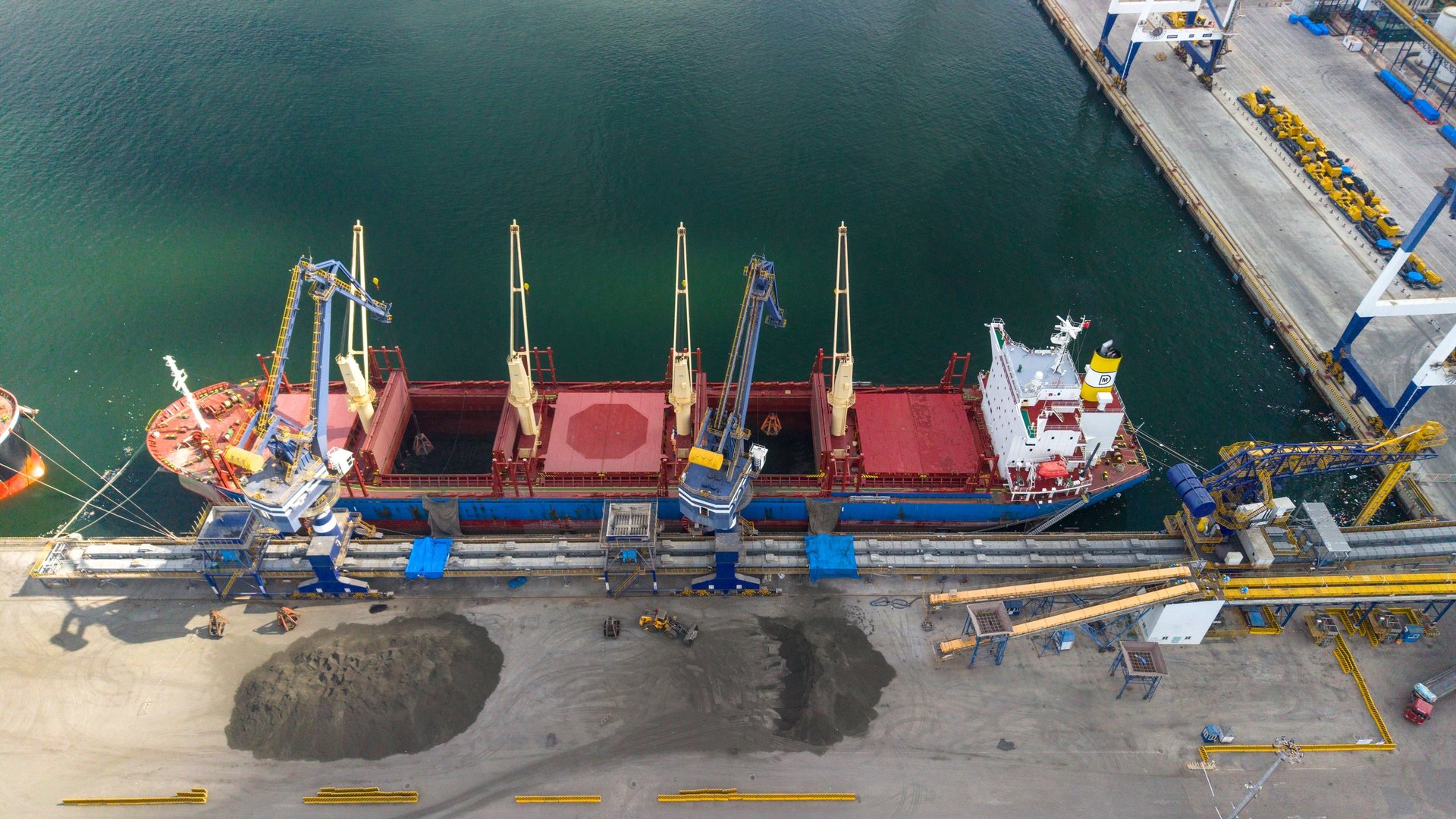 Bulk cargo vessel at a port terminal with its holds open during loading or discharge.