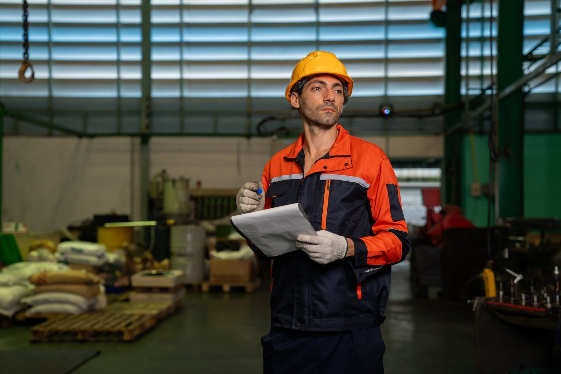 Technician in safety gear holding a checklist beside machinery during a quality check