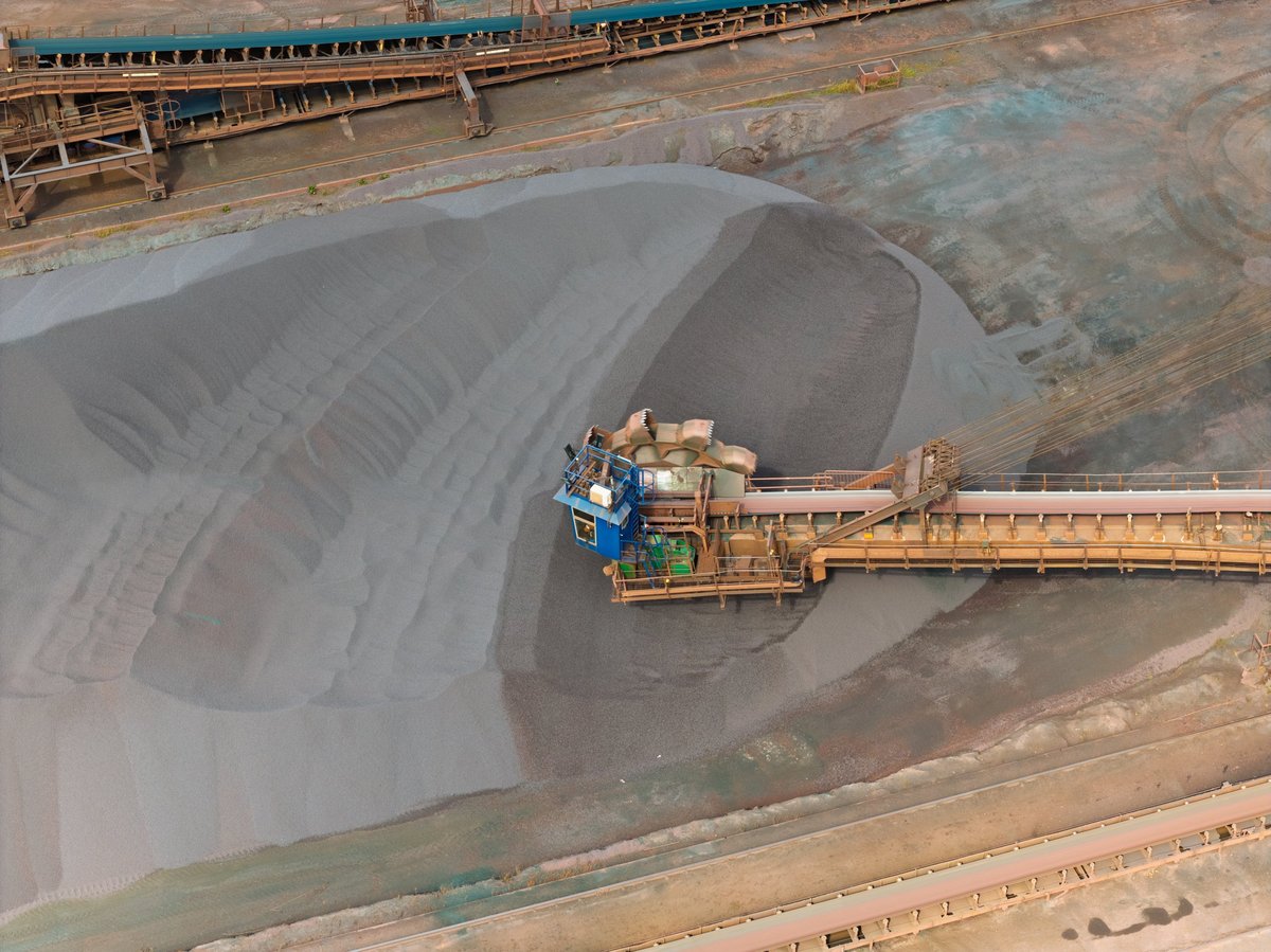Bulk handling equipment moving large stockpiles of iron ore material in an outdoor yard.