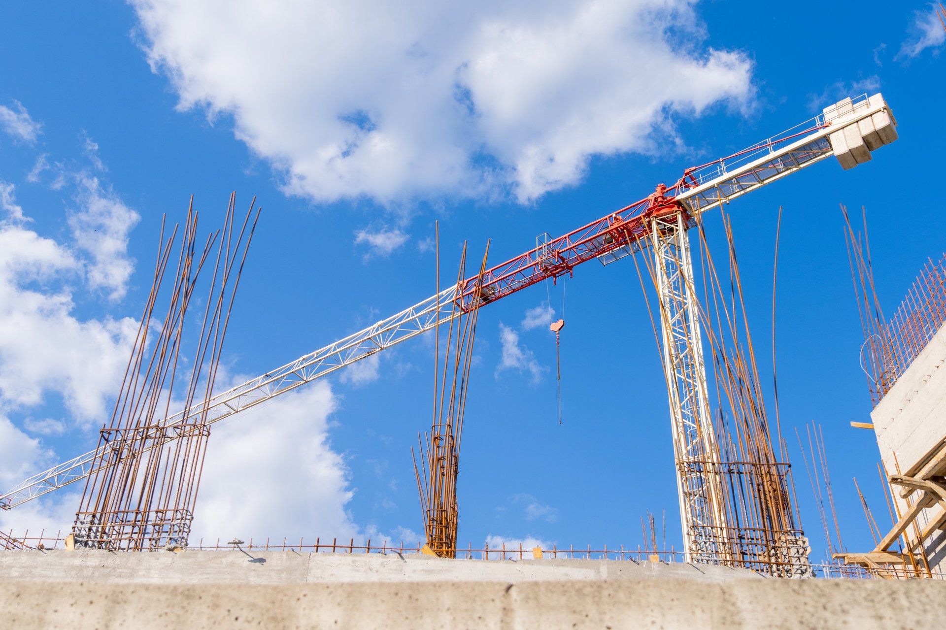 Tower crane with a hanging hook above steel rebar columns at a concrete building construction site, illustrating the members a 20 mm main-bar package is scheduled for.